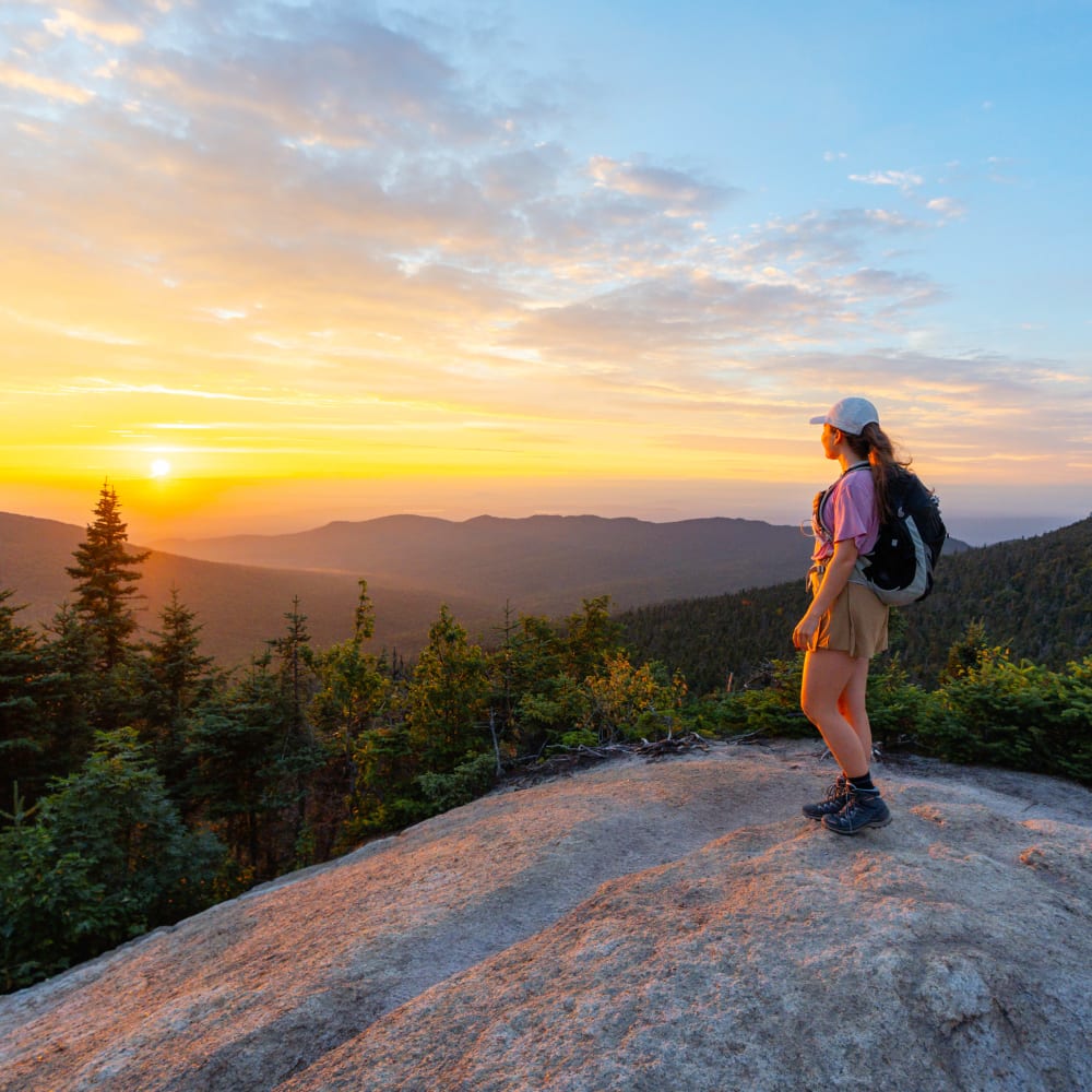 Femme au sommet d'une montagne qui regarde un coucher de soleil.