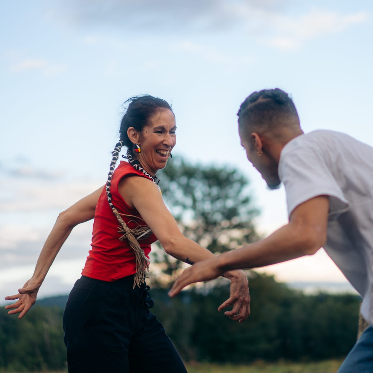 An Indigenous woman and a man have fun dancing outdoors