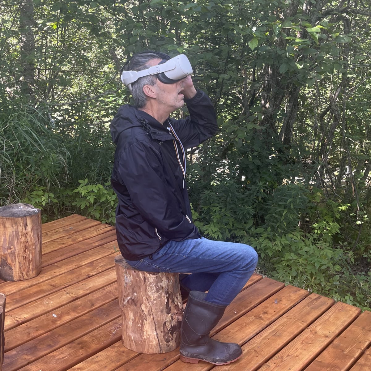 Malvina Center of Creation and Presentation Center - A man wearing a virtual reality headset sits on a tree stump in a wooded setting.