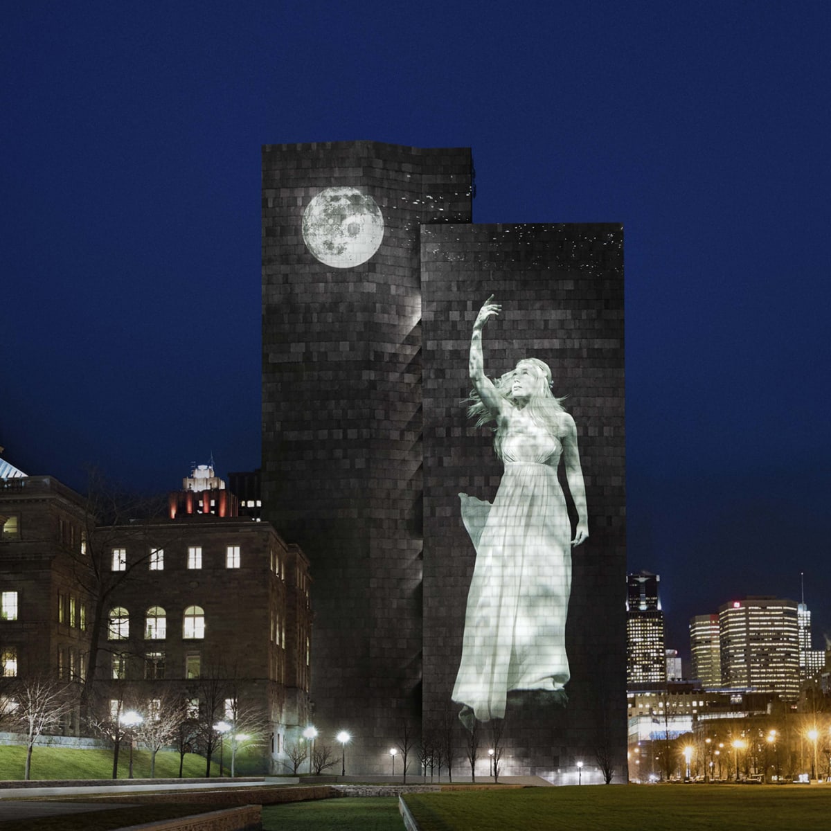 Cité Mémoire - Projection lumineuse d'une statue féminine et d'une lune sur un grand bâtiment sombre, la nuit