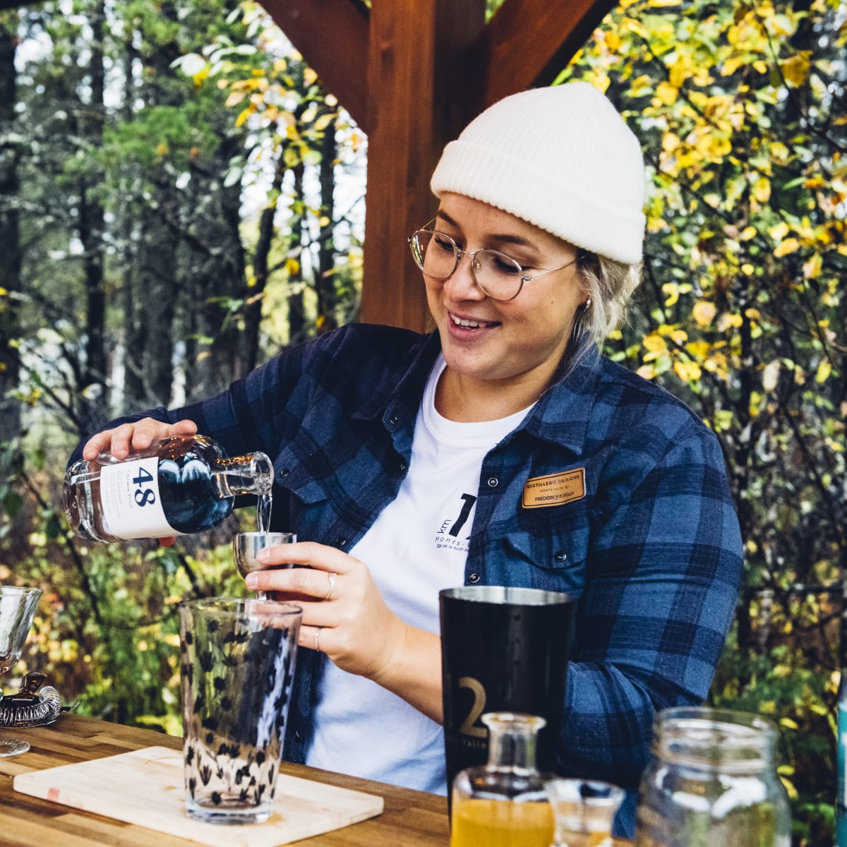 Distillerie du Fjord - Une femme prépare un breuvage alcoolisé, nature en arrière-plan.