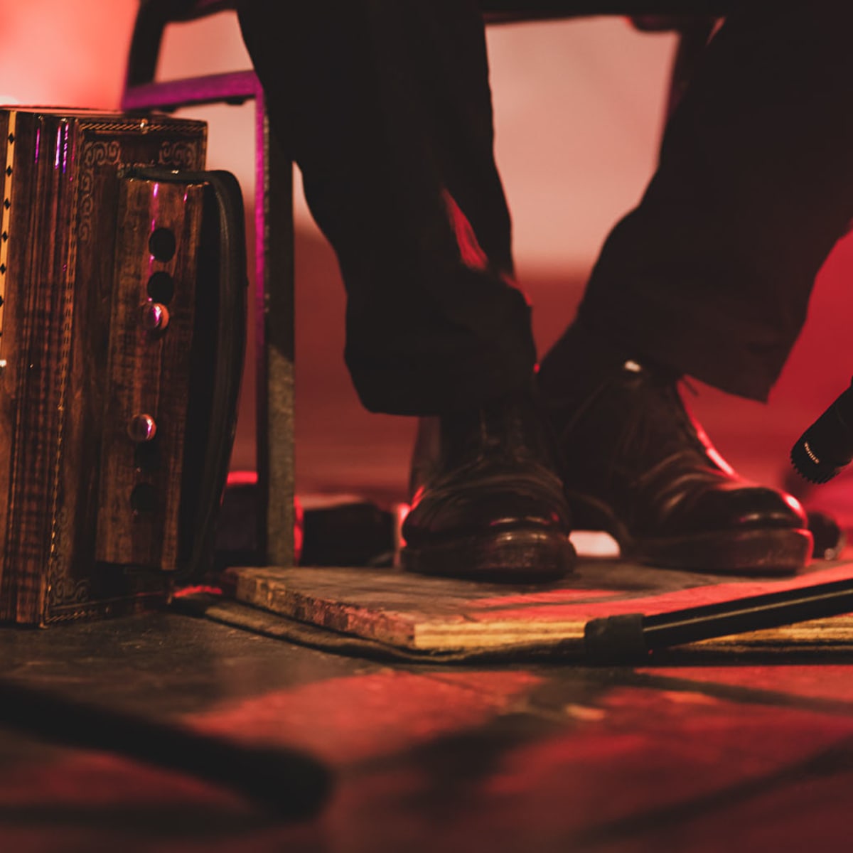 Festival de musique Trad Val-d'Or - Les pieds d'une personne assises sont chaussé de souliers noirs et sur une planche de bois, avec un micro en face. Un accordéon est à côté.