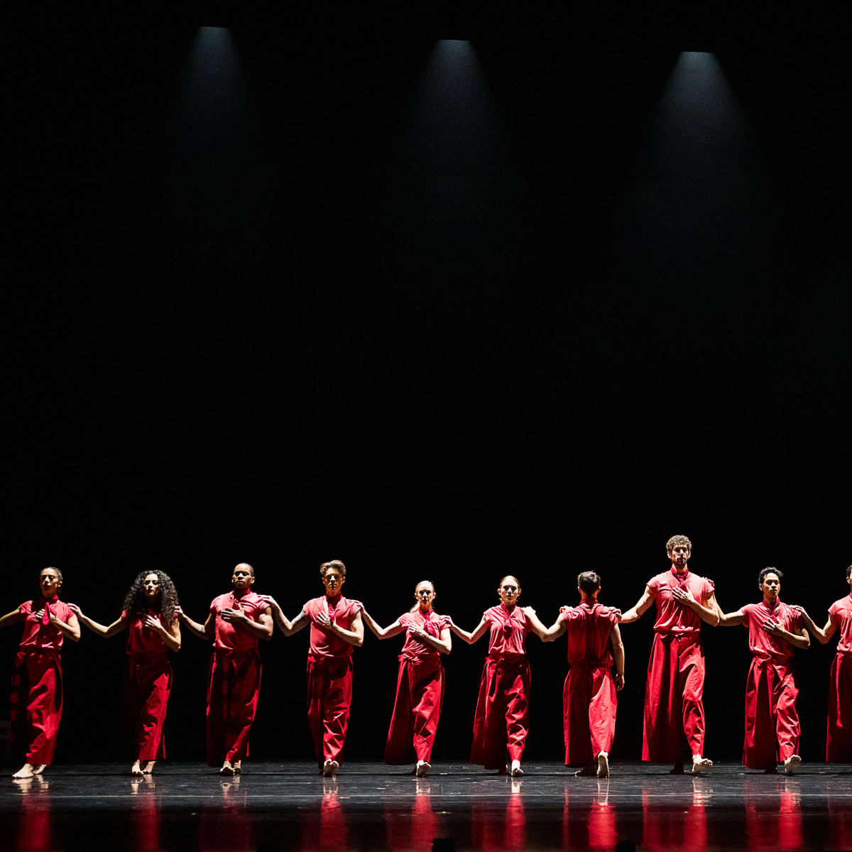 Festival des Arts de Saint-Sauveur - Des danseurs habillés en rouge sont disposés en ligne sur une scène noire