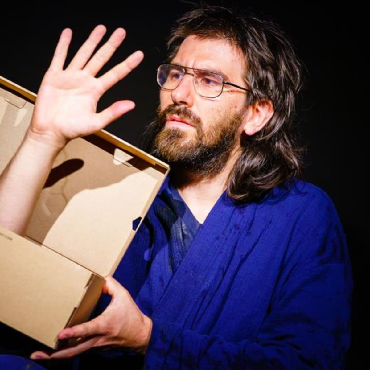 Festival international des arts de la marionnette -  A man looks at an arm sticking out of a shoebox.