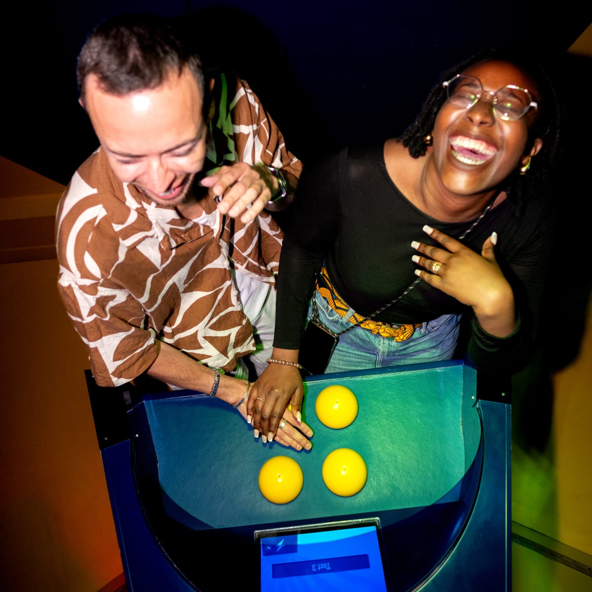 La Boîte à Questions – Quiz Room Montréal - Two people happily leaning over an interactive machine