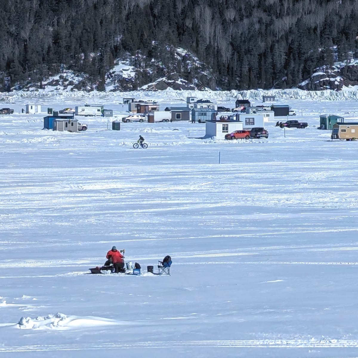 Le fjord du Saguenay enneigé avec des cabanes de pêche qu'on aperçoit au loin.