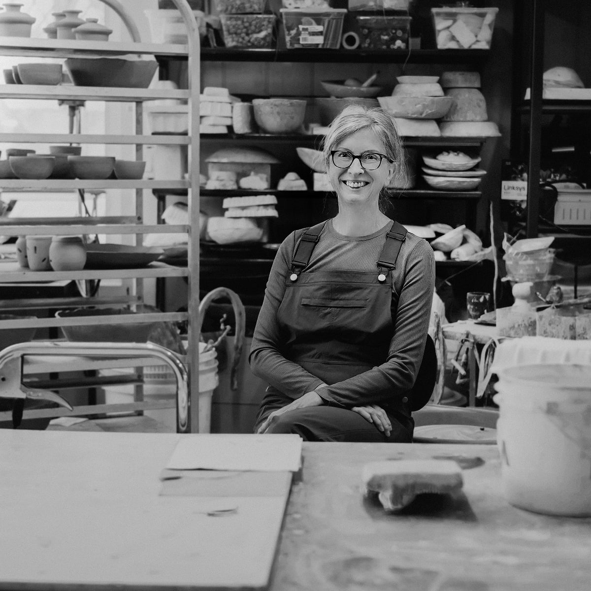 Artisane en céramique dans son atelier avec des créations autour d'elle.
