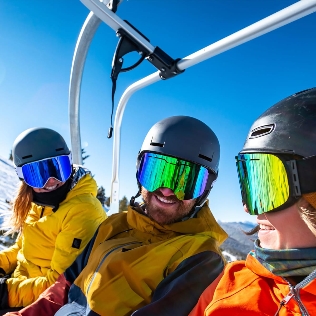 Three skiers in a lift, it's a sunny day and they're smiling.