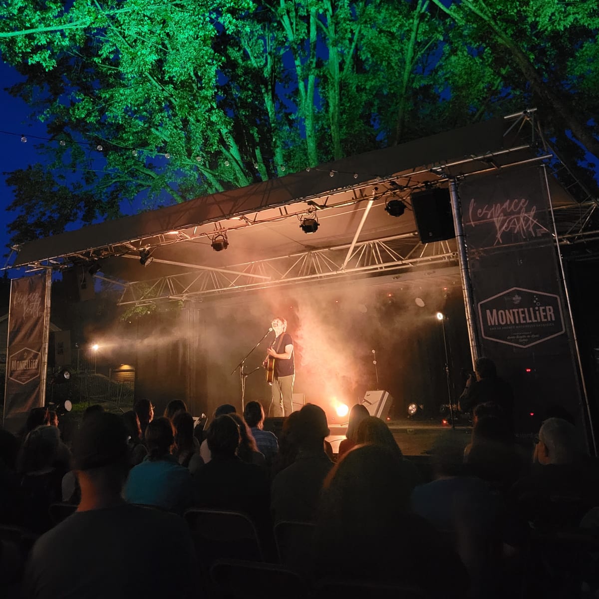 Stage with musical artist seen from the crowd, in the evening.