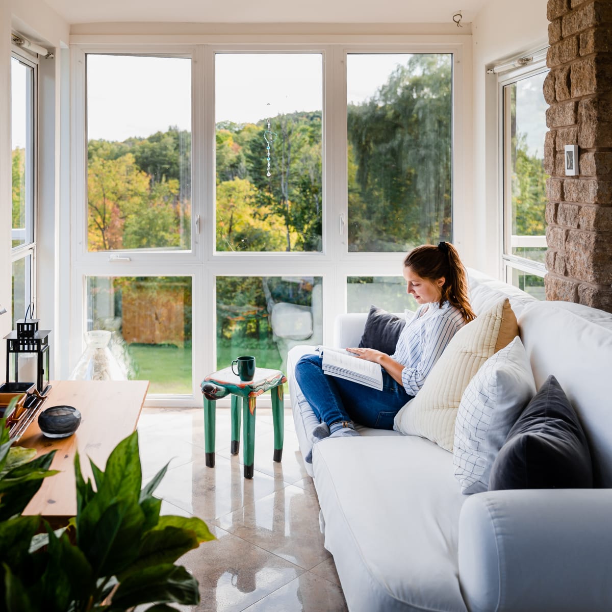 Femme installée sur un divan en train de lire dans une pièce bien fenestrée.