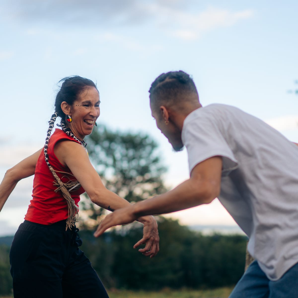 An Indigenous woman and a man have fun dancing outdoors