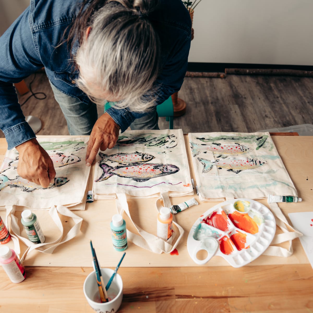 An Indigenous woman paints fish on a cloth