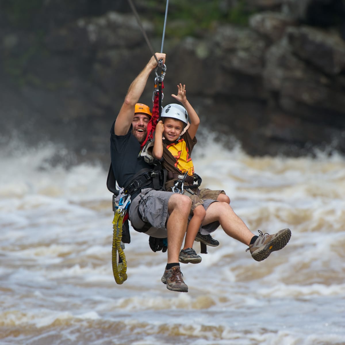 A man and a young boy on a zip line over a river. 