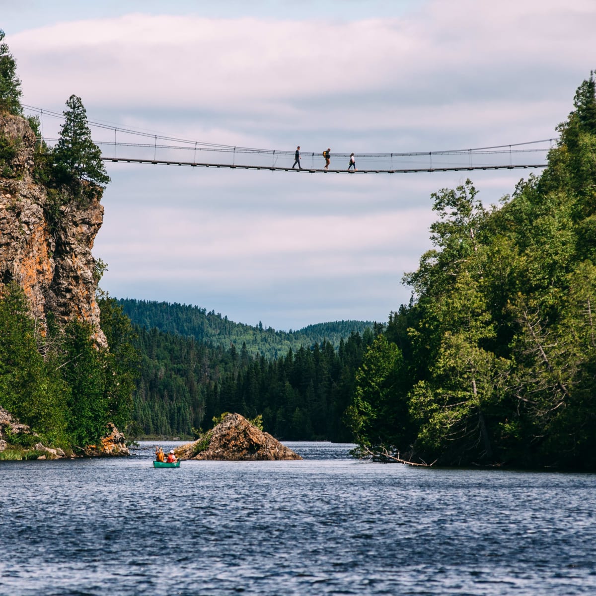 Suspension bridge over a body of water; there are people on the bridge and a boat on the water.