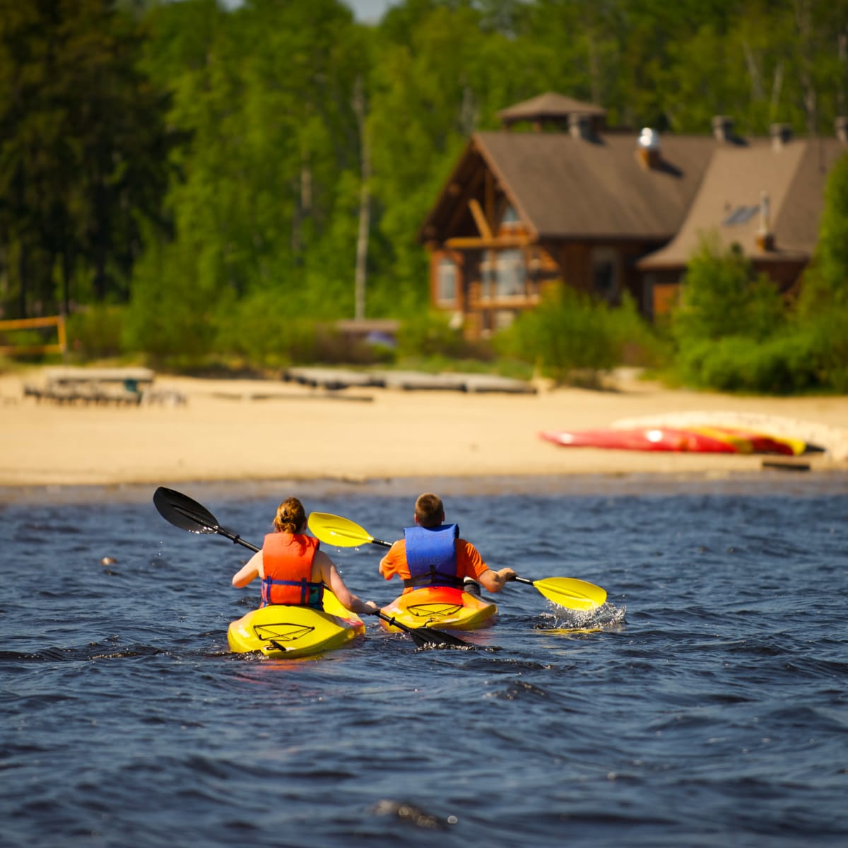 Two people kayaking on a stretch of water bordered by a sandy beach.