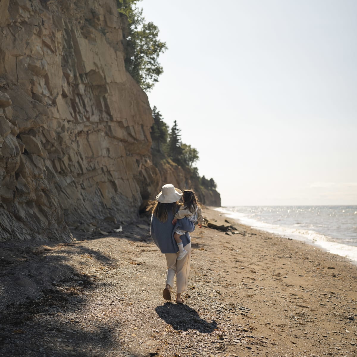 Mother and child on a beach bordered by a rocky outcrop.