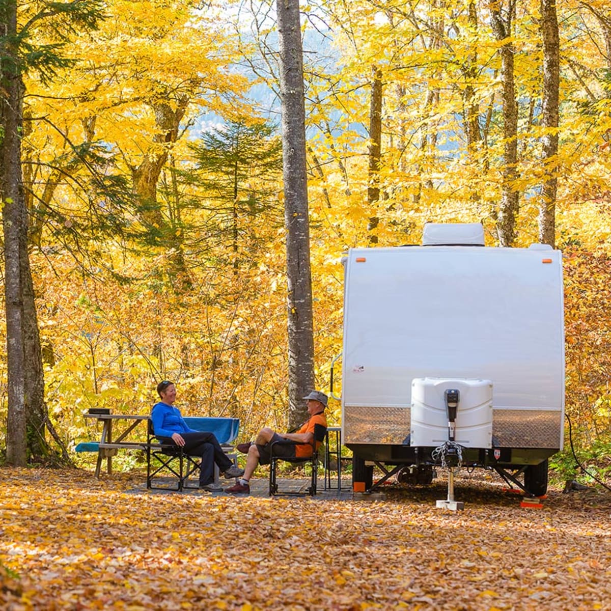 Two people sitting next to an RV in Parc national de la Jacques-Cartier in the fall.