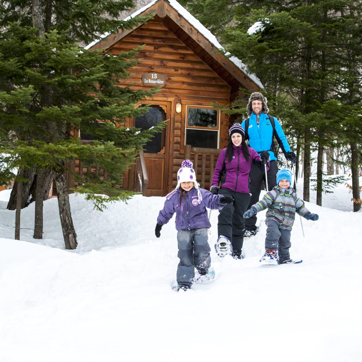 A family on snowshoes in front of a cabin at Sommet Morin Heights.