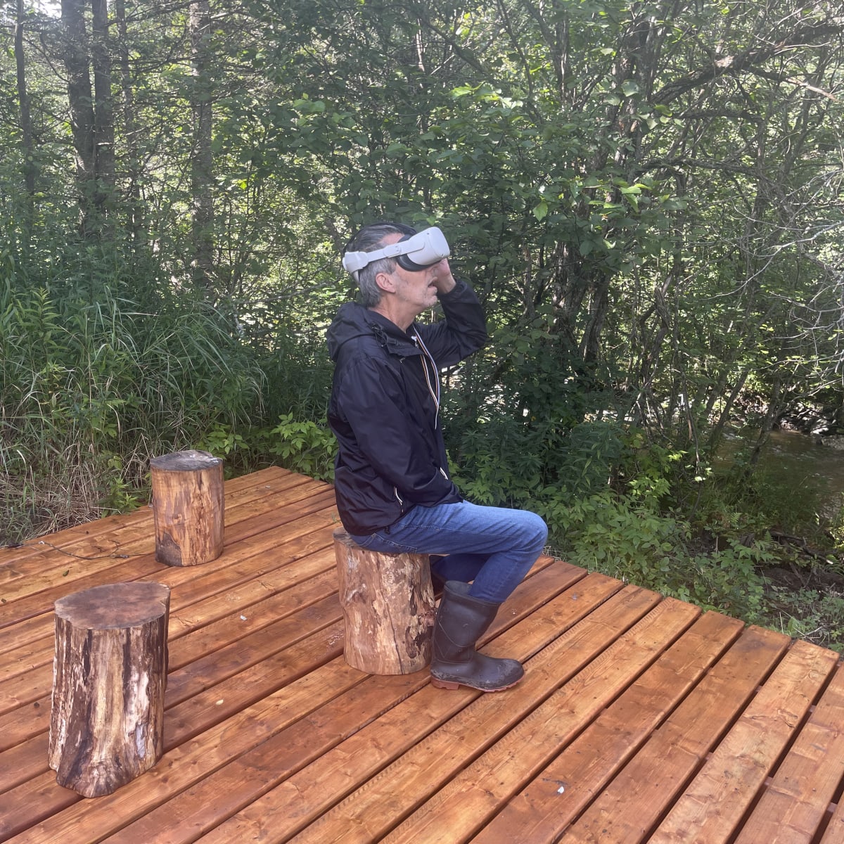 Malvina Center of Creation and Presentation Center - A man wearing a virtual reality headset sits on a tree stump in a wooded setting.