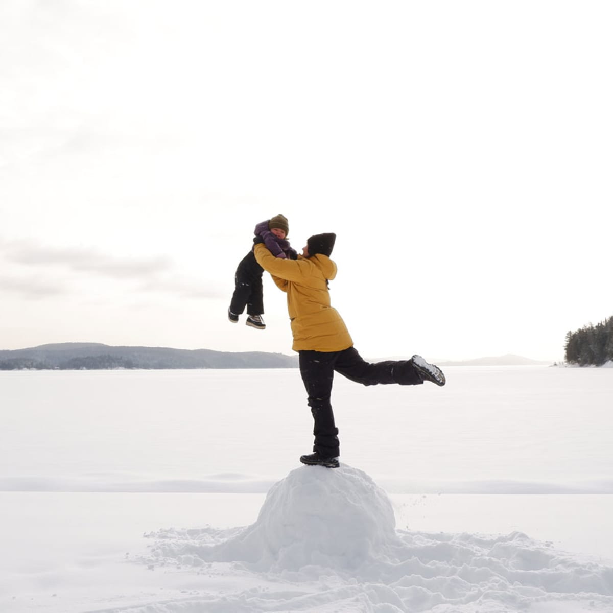 A parent holding their child in the air at the Centre touristique du Lac-Simon, in winter.