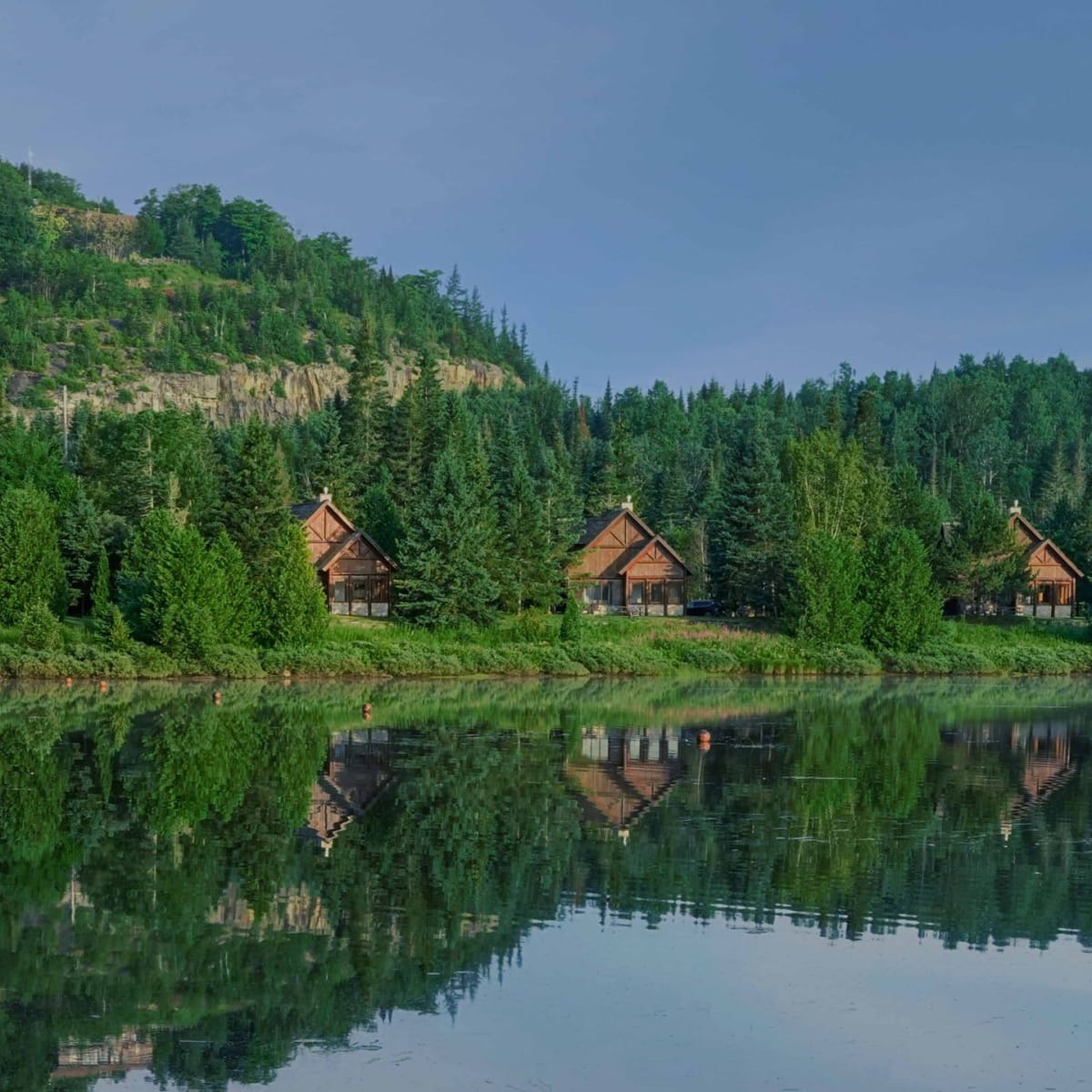 A row of five cottages on the shore of a lake in the lush green landscape of Chalets Royal Laurentien.