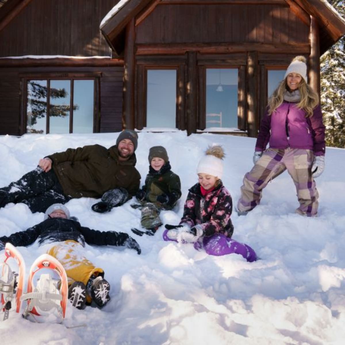 Famille couchée dans la neige devant un chalet.