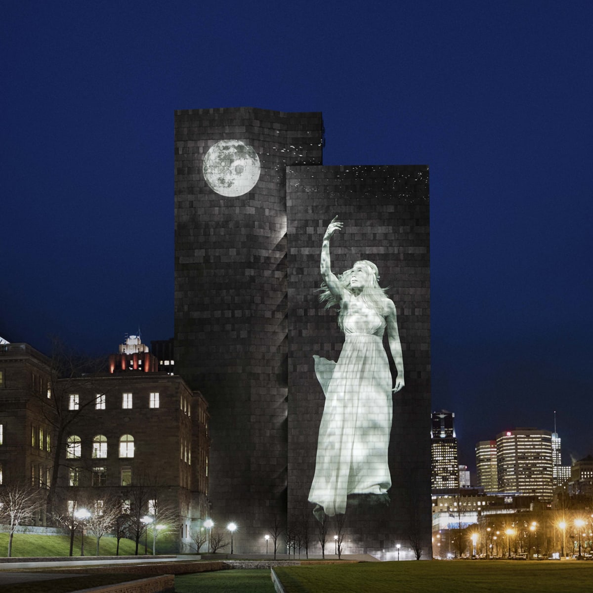 Cité Mémoire - Light projection of a woman and a moon on a large dark building, at night