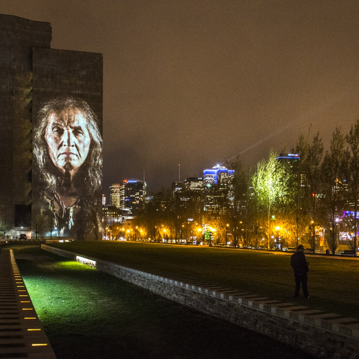 Cité Mémoire - Light projection of an individual on a large dark building at night