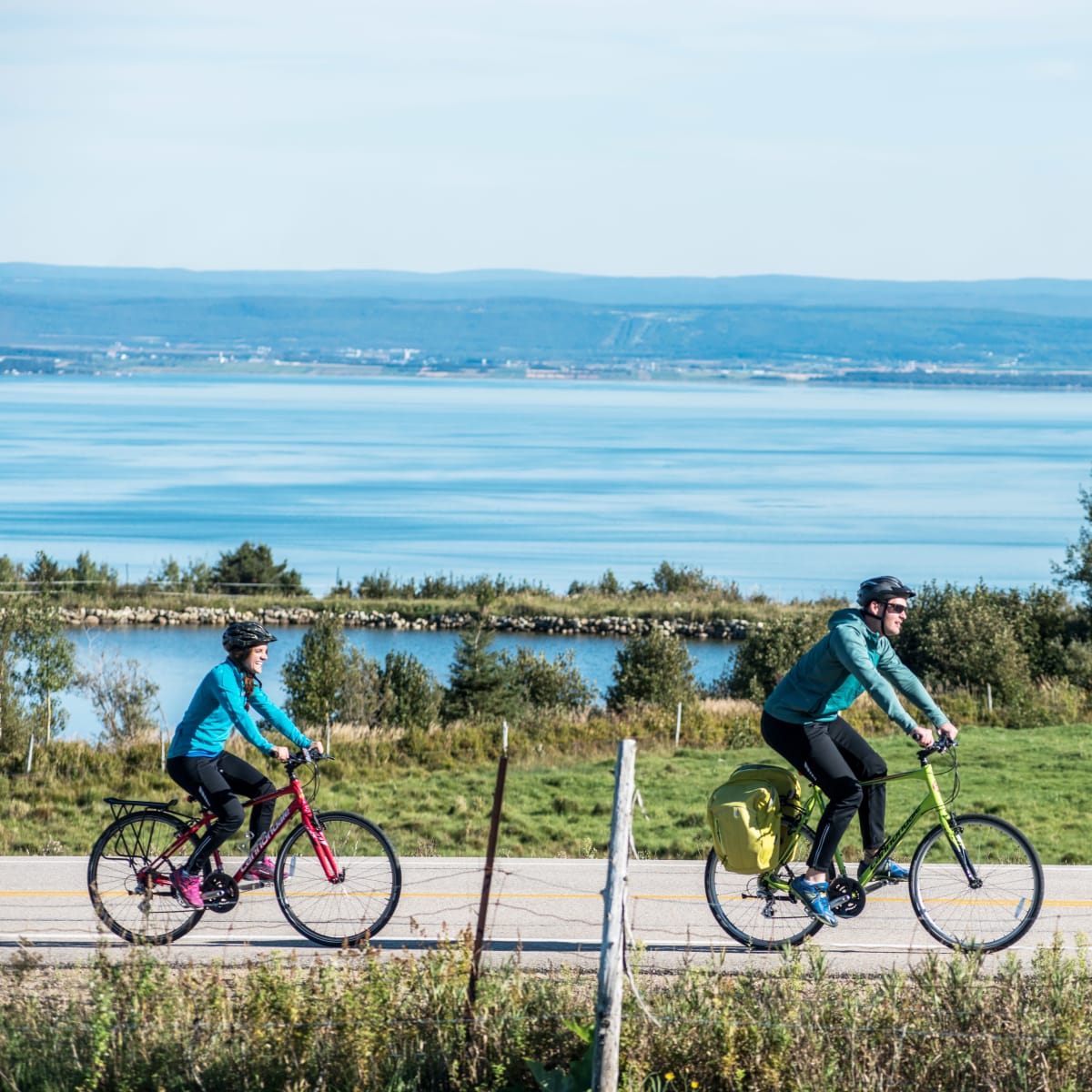 Two cyclists exploring the Charlevoix region by bike, with the St. Lawrence River in the background.