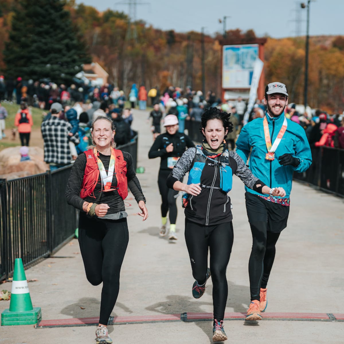 Défi des Couleurs Simard - Three people cross the finish line of a race, with a crowd in the background.