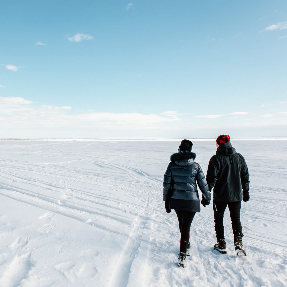 Couple holding hands on the frozen and snow-covered Lac Saint-Jean, in sunny weather.