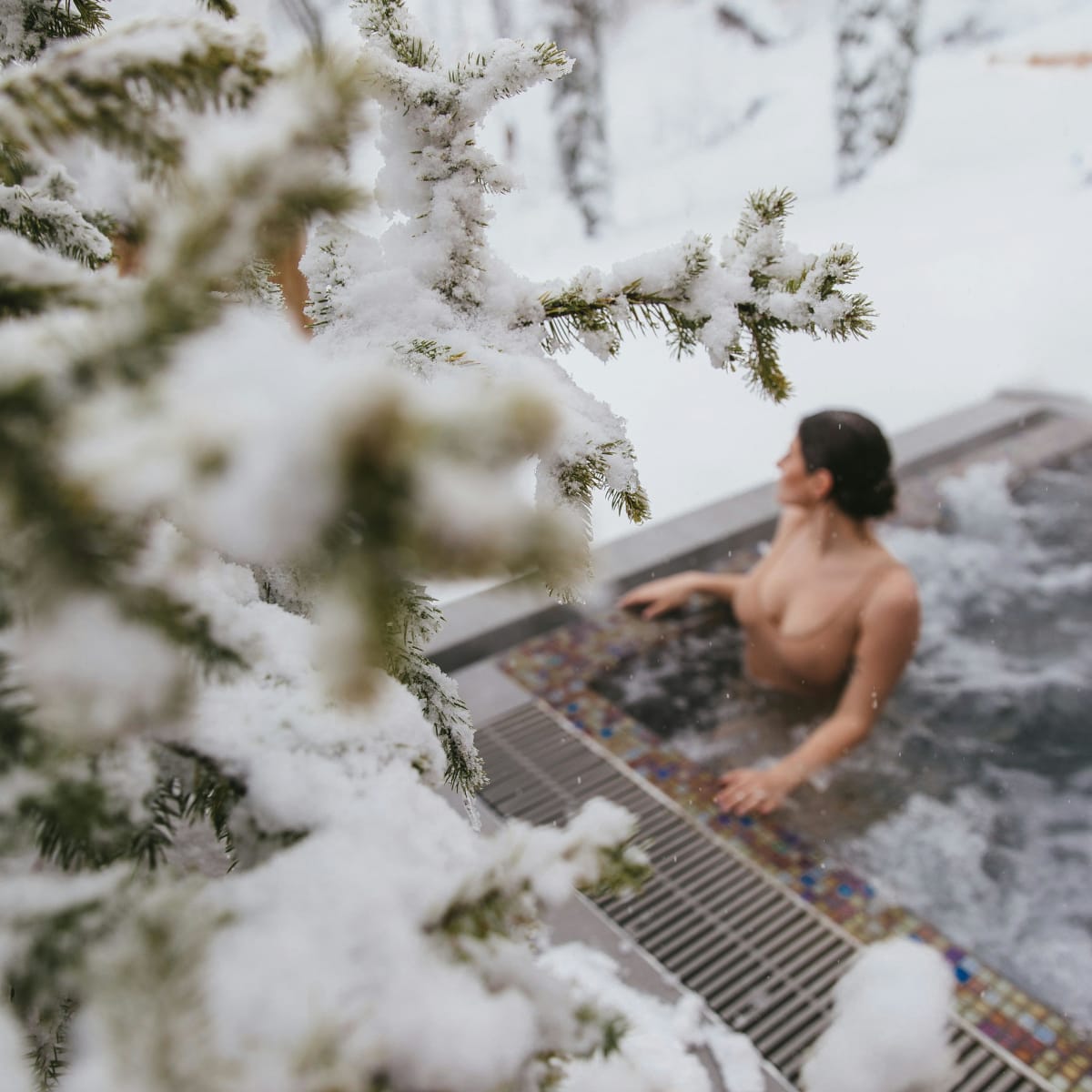 Woman in an outdoor spa; around her, there are snow-covered trees.