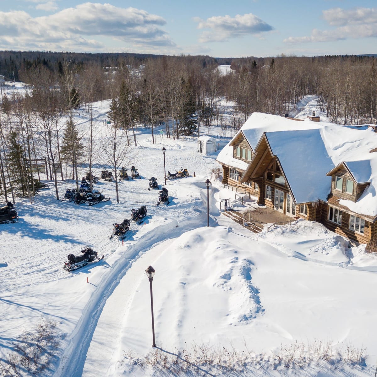 Vue aérienne du Centre sportif Le Jasmin sous la neige, avec motoneiges stationnées à proximité.