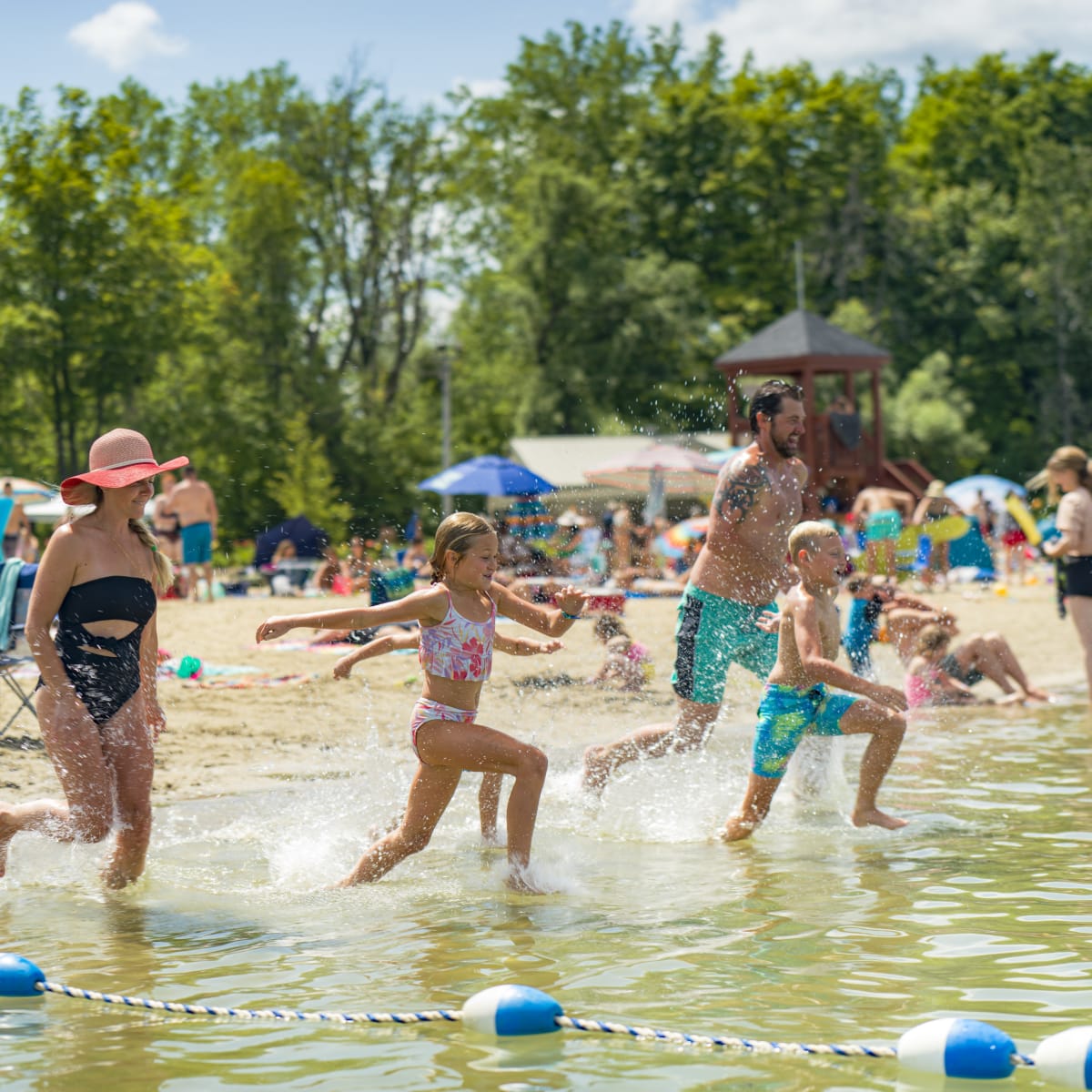 Family running toward the water at the beach in Îles-de-Saint-Timothée Regional Park