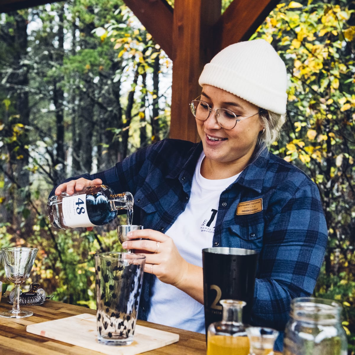 Distillerie du Fjord - A woman prepares an alcoholic beverage, nature in the background.
