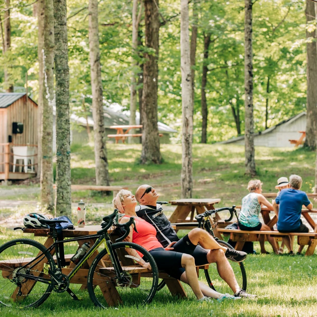Érablière du Village - A man and a woman are seated at a picnic table, with their bikes leaning against it.
