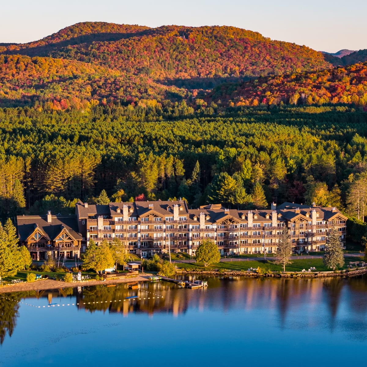 Aerial view of the Grand Lodge Mont-Tremblant, with a lake in the foreground and colourful mountains in the background.