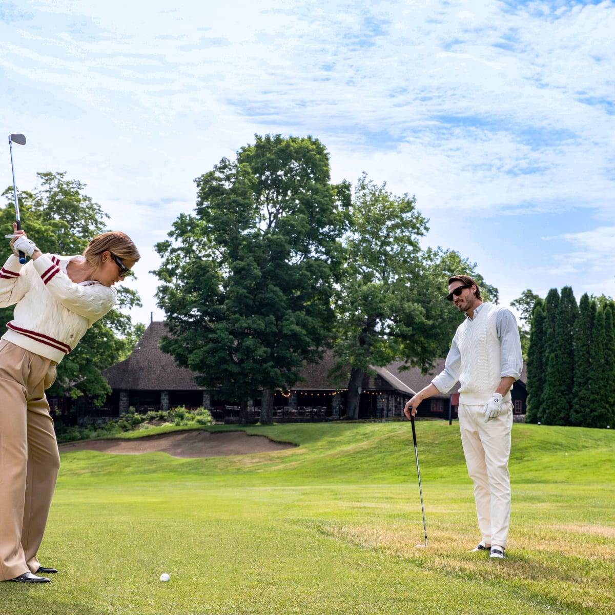 Deux personnes sur un terrain de golf; une s'élance, l'autre observe.