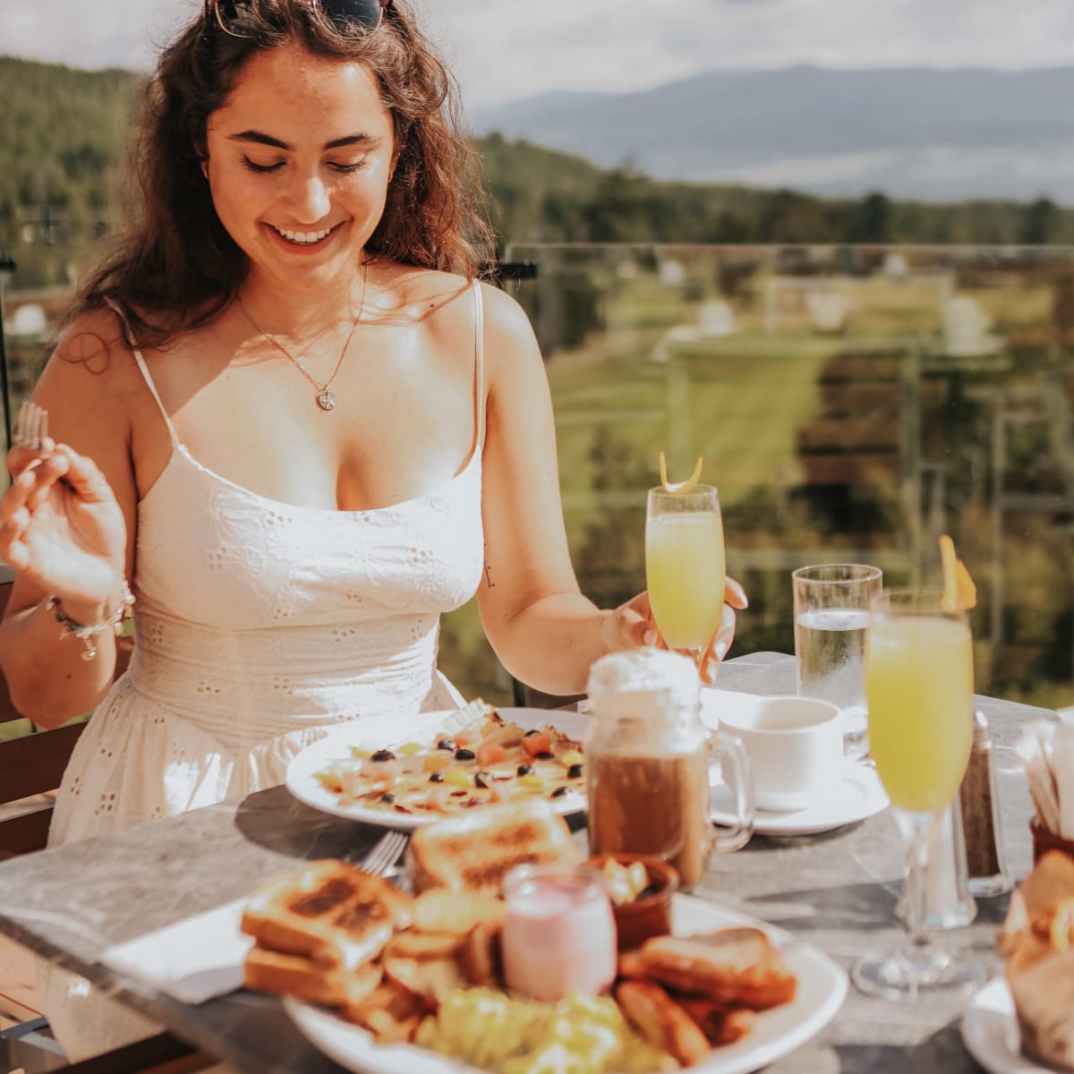 A smiling woman on a terrace with plates piled high on the table in front of her.