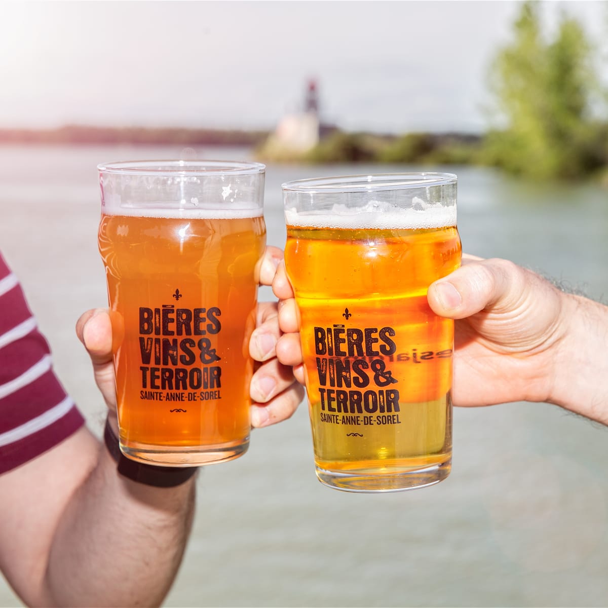 Deux mains qui trinquent avec des bières au bord de l'eau.