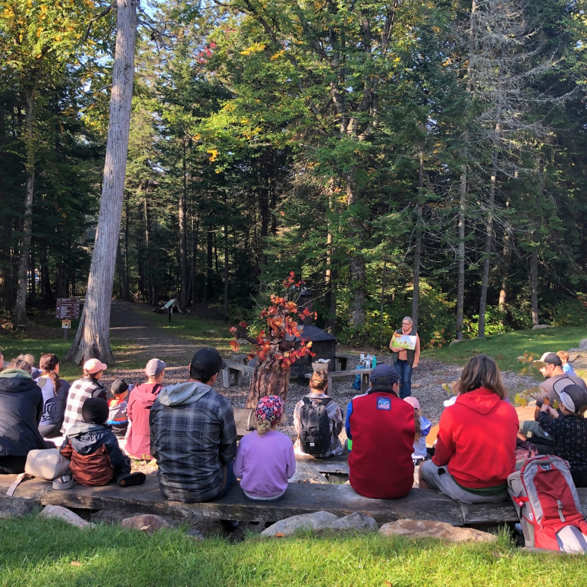A group is sitting and watching a presenter at the “Festival des Couleurs” at Parc régional Montagne du Diable.