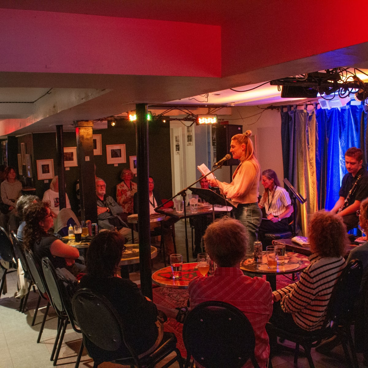 People seated in a room with a woman speaking into a microphone.