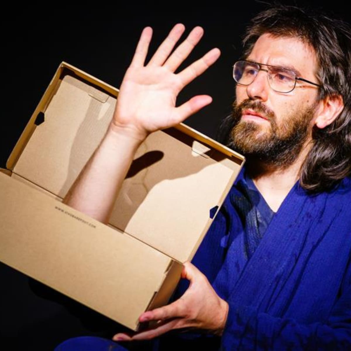 Festival international des arts de la marionnette -  A man looks at an arm sticking out of a shoebox.