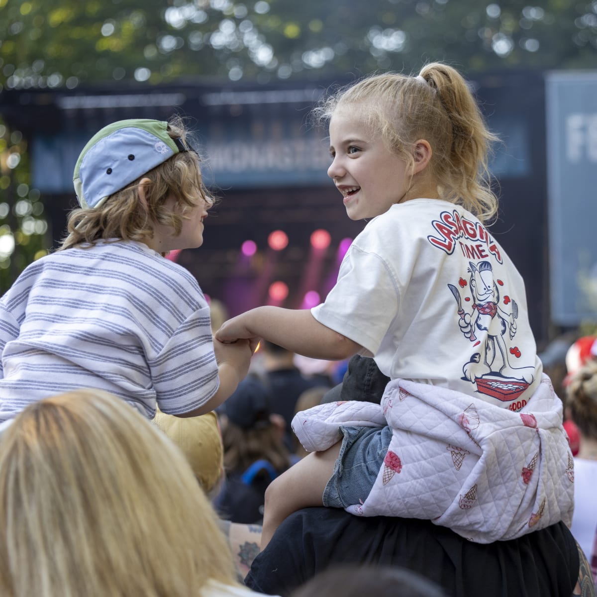 Two children sitting on the shoulders of adults at the FestiVoix de Trois-Rivières.