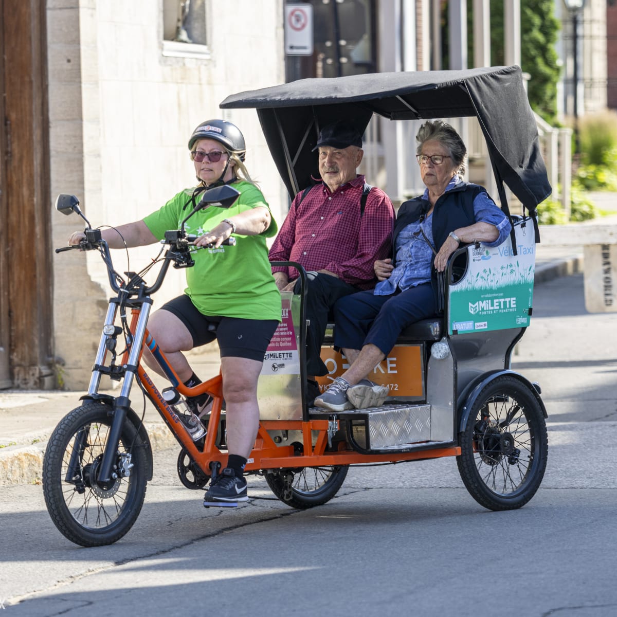 Two adults are being transported by bicycle taxi to the FestiVoix festival in Trois-Rivières.