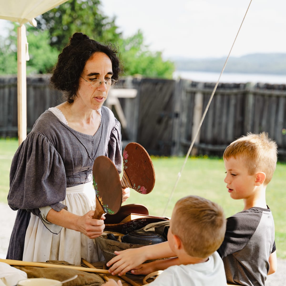 A woman in period costume interacting with two young boys.