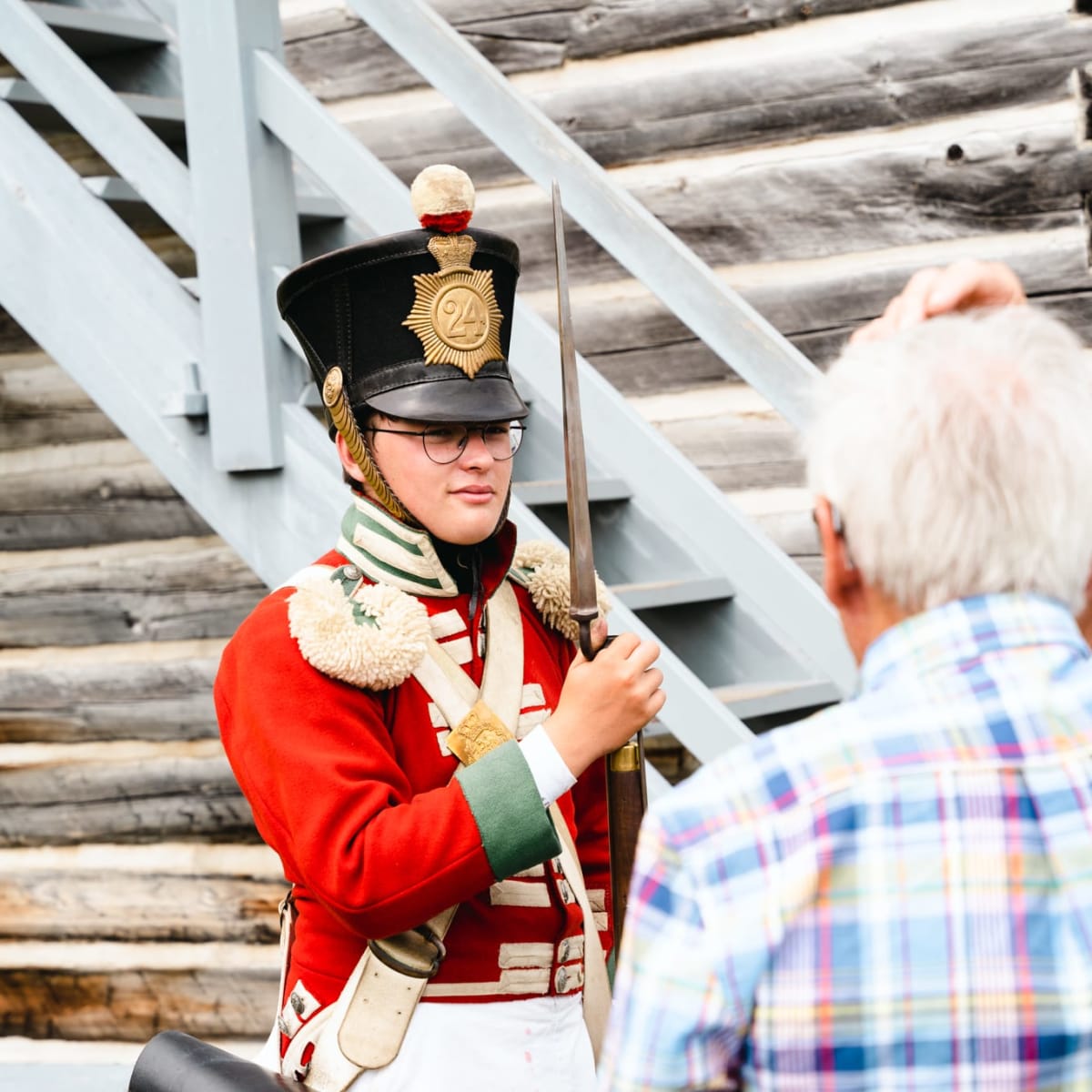 A soldier in a red uniform standing in front of an elderly man.