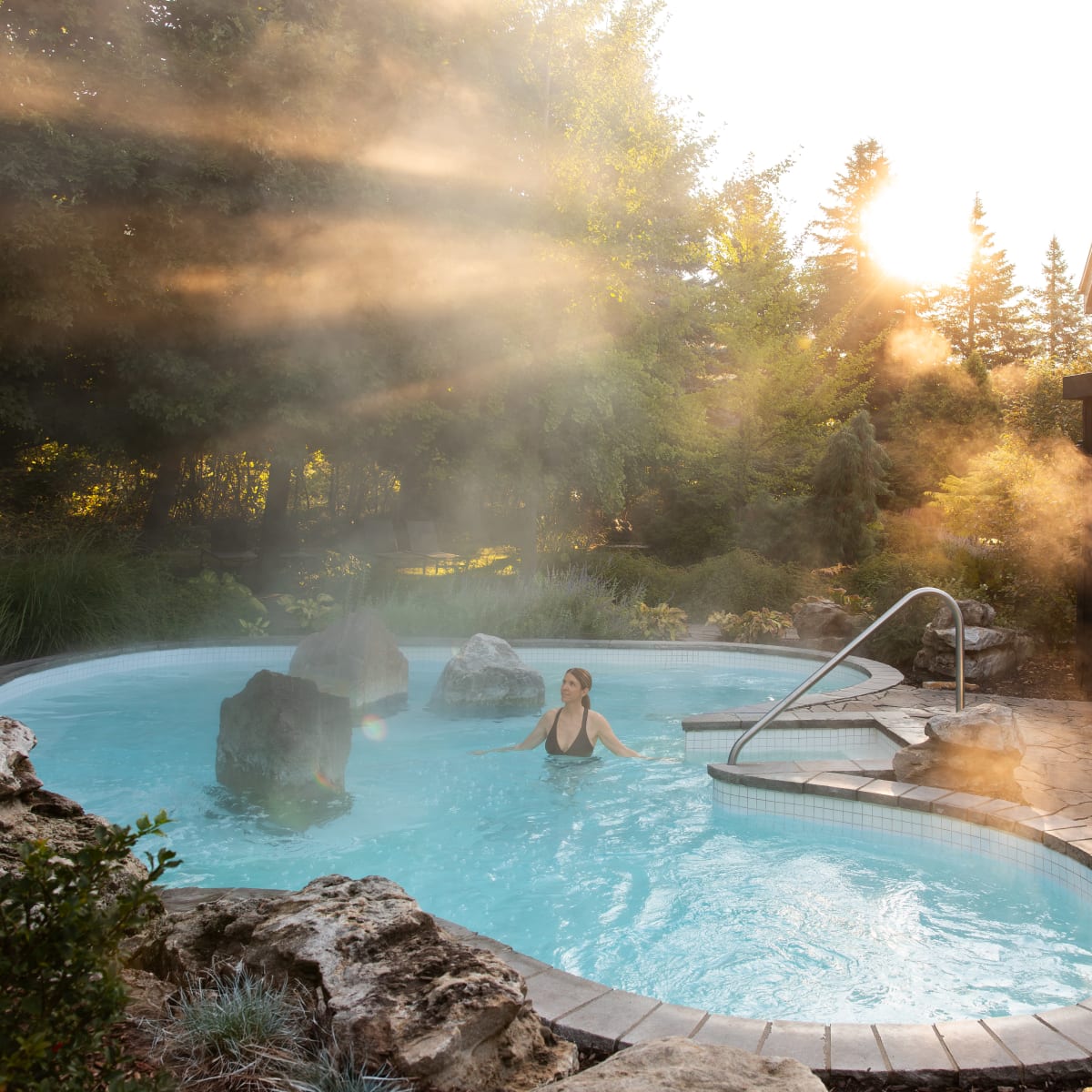 Une personne se détend dans un bain thermal entouré de nature au coucher de soleil.