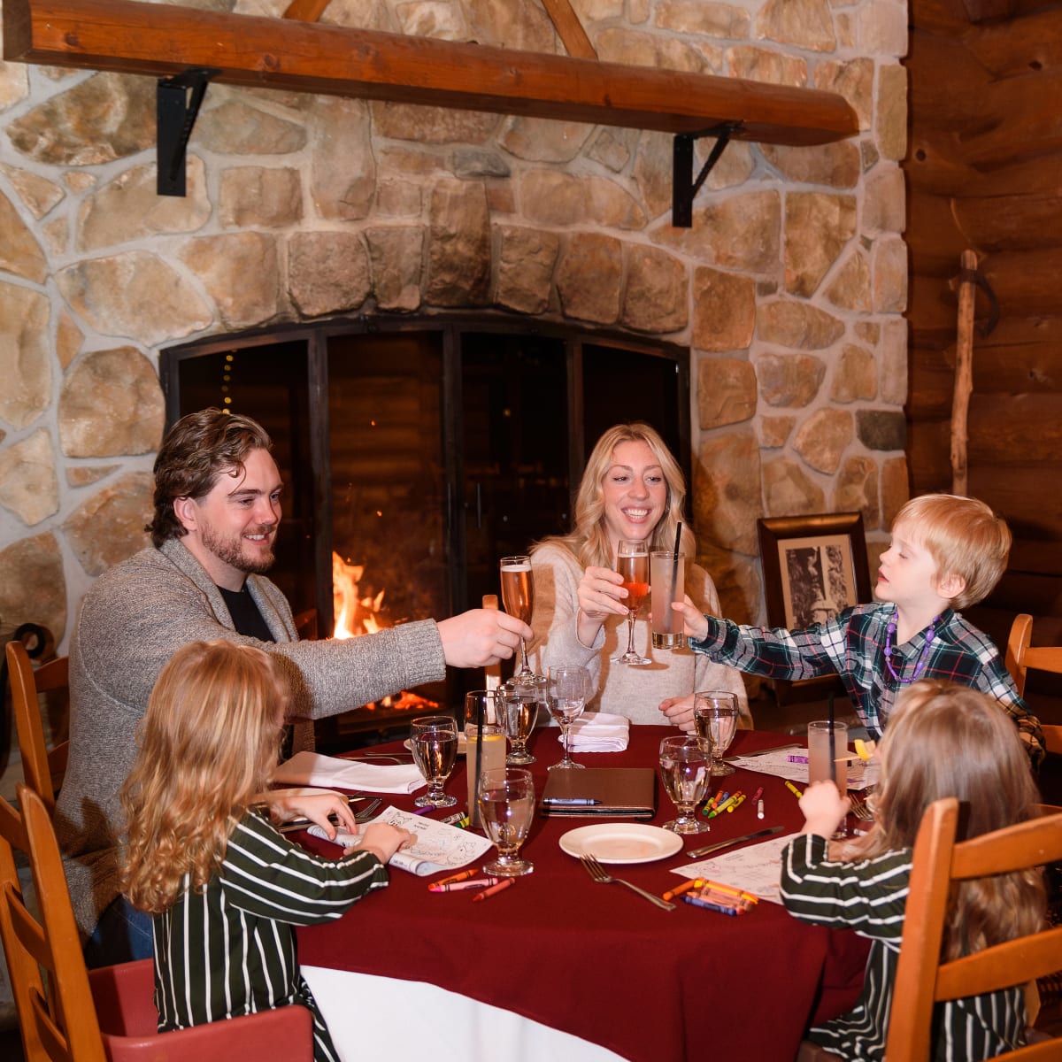 Two parents and three children seated at a table in a rustic setting.
