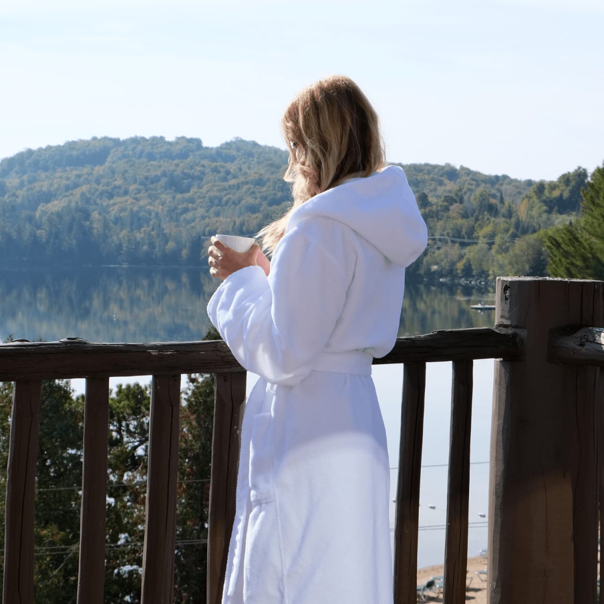 Une jeune femme en robe de chambre buvant son café sur le balcon.